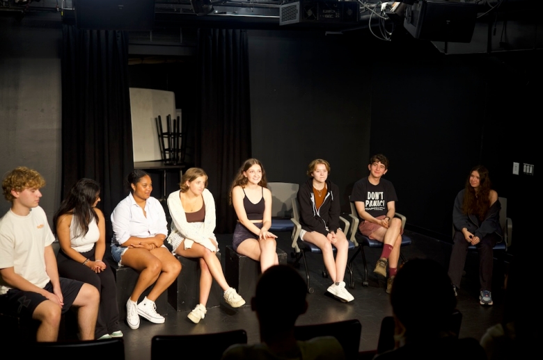 Photo of students sitting on chairs on stage in a Tisch classroom auditorium